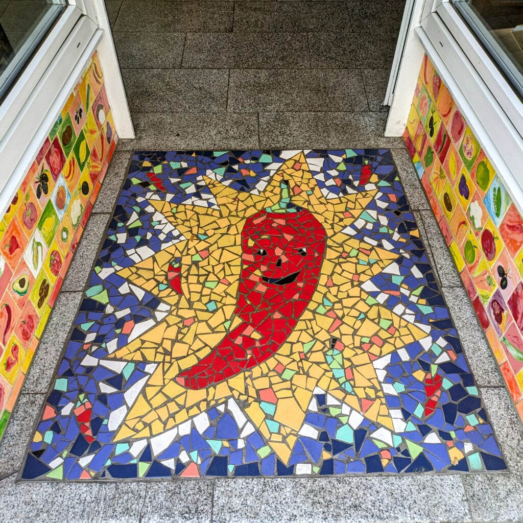 Die Peperoni Gemüsekultur präsentiert sich als eine kulinarische Oase im pulsierenden Herzen von Münster, die eine exquisite Fusion aus persischer, mediterraner und orientalischer Küche auf den Tisch zaubert. Schon beim Näherkommen wird man von den bunten Kacheln dieses charmanten Gemüseladens magisch angezogen. Sobald du vor der Tür stehst, umfängt dich der verführerische Duft orientalischer Gewürze, der deine Sinne in eine andere Welt entführt. Ein neugieriger Blick durch die Fenster offenbart eine warme, einladende Atmosphäre, in der Gäste zwischen frischem Gemüse und Obst sitzen und das reichhaltige vegetarische Buffet Günstig essen in Münster
