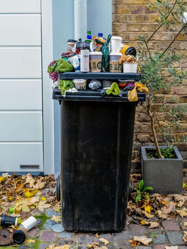schwarze Mülltonne mit grünen Blättern und Müll
