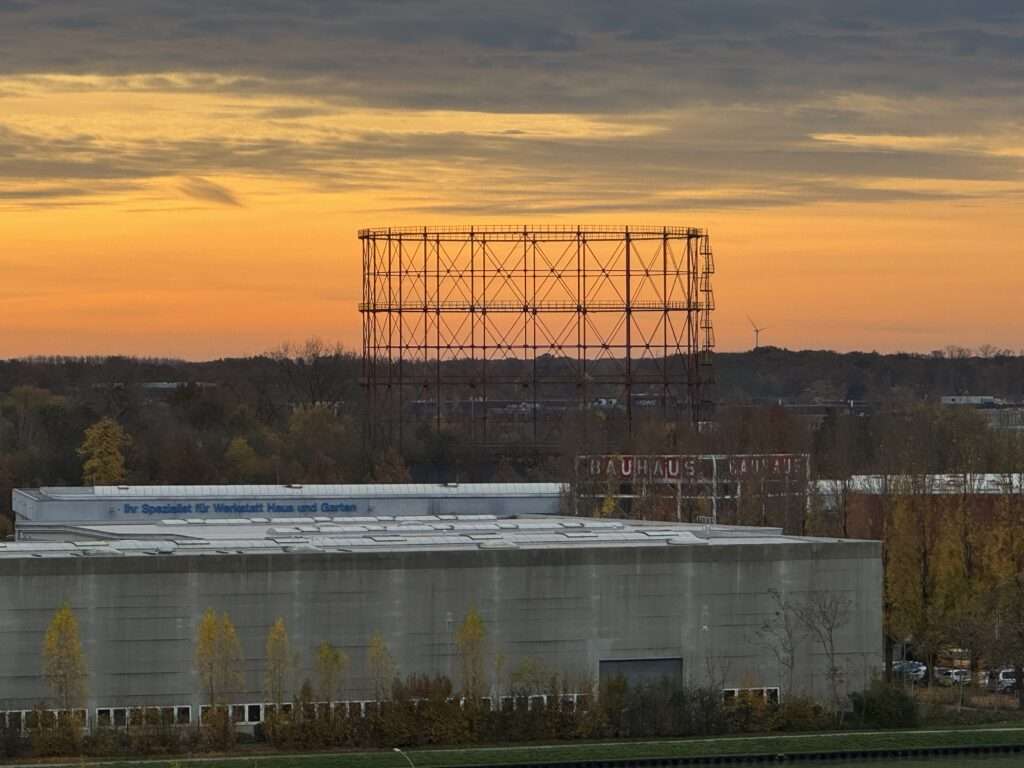 Das ambitionierte Bauvorhaben am Albersloher Weg steht vor einem grundlegenden Neustart. Die bisherigen Planungen für das sogenannte Gasometer-Projekt in Münster sind vom Tisch. Die CDU-Ratsfraktion wertet diese Entwicklung als „Scheitern mit Ansage“ und sieht darin ein Signal für grundsätzliche Probleme in der städtischen Baupolitik. Fraktionschef Stefan Weber erklärte, nun beginne „wieder alles von vorne“. Für die Christdemokraten ist das vorläufige Aus nicht überraschend, sondern Folge struktureller Rahmenbedingungen, die Investitionen zunehmend erschwerten. Geplantes Vorzeigeprojekt mit 14 Geschossen Im denkmalgeschützten Gerüst des ehemaligen Gasometers sollte ein 14-geschossiger Zylinderbau entstehen. Vorgesehen war ein „vertikales Stadtquartier“ mit einer Mischung aus Wohnen, Gewerbe und kulturellen Angeboten. Der Rat hatte 2025 mit dem Bebauungsplan Nr. 626 die planungsrechtliche Grundlage geschaffen. Die Vorhabenträgerin UTB Projektmanagement hat nun die bisherigen Entwürfe zurückgezogen. Als Begründung werden erhebliche Kostensteigerungen genannt. Statt des ursprünglichen Konzepts sollen zwei einfachere Alternativen geprüft werden. Der Nutzungsmix soll nach bisherigen Informationen grundsätzlich erhalten bleiben, allerdings in veränderter baulicher Form. Steigende Baukosten als zentraler Faktor Das Gasometer-Projekt steht nicht isoliert da. Bundesweit sind Bauvorhaben durch steigende Kosten unter Druck geraten. Nach Angaben des Statistischen Bundesamtes lagen die Baupreise für konventionelle Wohngebäude im November 2025 um 3,2 Prozent höher als im Vorjahr. Gleichzeitig berichten Branchenverbände und Wirtschaftsforschungsinstitute von einem anhaltenden Auftragsmangel im Wohnungsbau. Auch die Zahl der Baugenehmigungen ist rückläufig. Die angespannte Finanzierungslage, hohe Zinsen sowie volatile Material- und Energiekosten führen dazu, dass Investoren Projekte verschieben oder neu kalkulieren müssen. CDU sieht strukturelle Probleme in Münster Für die CDU ist das vorläufige Aus des Projekts jedoch nicht allein auf die konjunkturelle Lage zurückzuführen. Stefan Weber spricht von „überzogenen Vorstellungen“ und zu hohen Standards, die Bauvorhaben zusätzlich verteuerten. In der aktuellen wirtschaftlichen Situation müsse man sich von sogenannten Goldstandards verabschieden, um Bauen wieder wirtschaftlich möglich zu machen. CDU-Vize Mathias Kersting warnt vor langfristigen Folgen: Ohne ein Umdenken drohe Münster als wachsende Stadt an Dynamik zu verlieren. Tausende preisgünstige Wohnungen könnten schneller entstehen, wenn Verfahren beschleunigt, Flächen mobilisiert und kostentreibende Vorgaben reduziert würden.